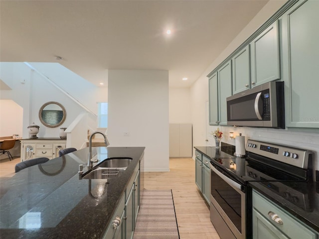 kitchen featuring appliances with stainless steel finishes, a sink, green cabinetry, light wood-style flooring, and recessed lighting