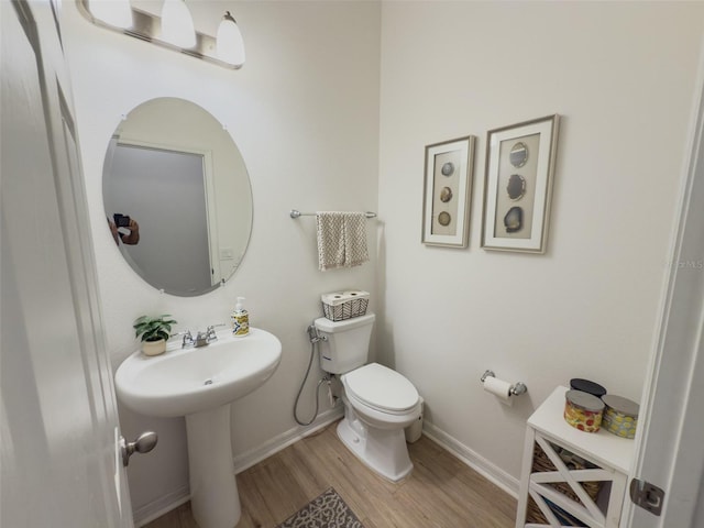 bathroom featuring wood finished floors, toilet, baseboards, and a sink