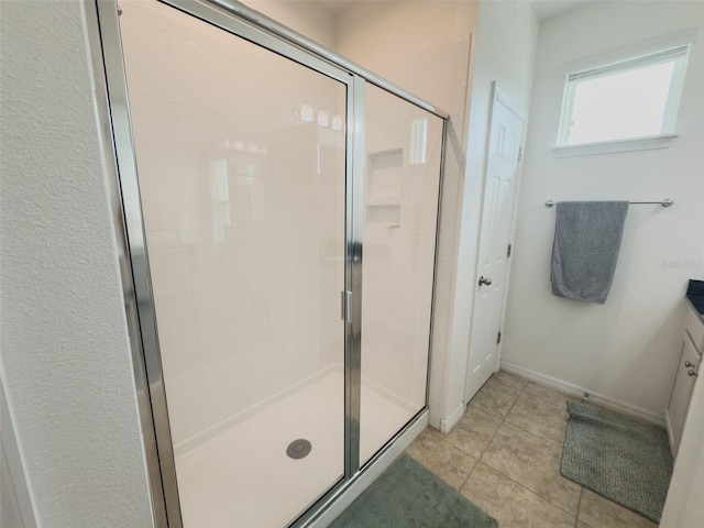 full bathroom with a stall shower, tile patterned flooring, baseboards, and vanity
