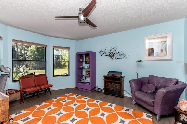 living area with wood finished floors, ceiling fan, a textured ceiling, and baseboards