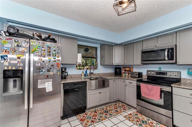 kitchen featuring stainless steel appliances, gray cabinets, a textured ceiling, a sink, and light tile patterned flooring