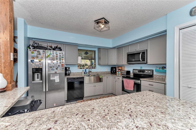 kitchen featuring appliances with stainless steel finishes, gray cabinetry, a sink, a textured ceiling, and light stone counters