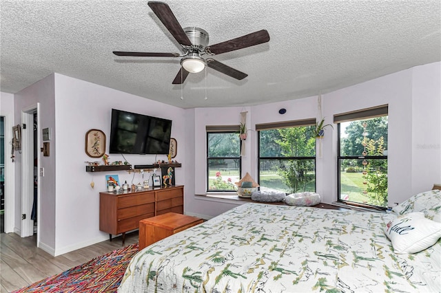 bedroom with a textured ceiling, wood finished floors, baseboards, and a ceiling fan