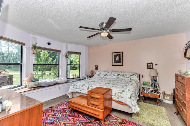 bedroom featuring a textured ceiling, multiple windows, wood finished floors, and a ceiling fan