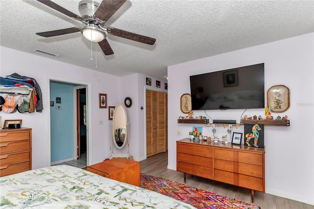 bedroom featuring a textured ceiling, wood finished floors, a closet, baseboards, and a ceiling fan