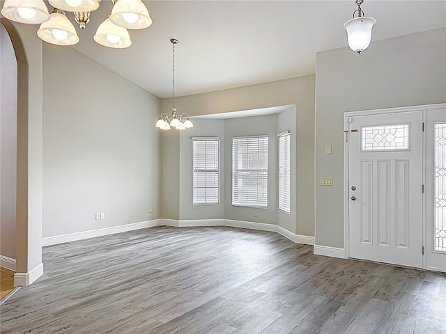 foyer entrance with arched walkways, an inviting chandelier, plenty of natural light, and wood finished floors