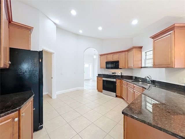 kitchen featuring a sink, dark stone counters, light tile patterned flooring, black appliances, and arched walkways