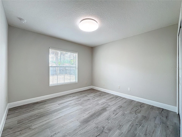 unfurnished room with a textured ceiling, baseboards, and wood finished floors
