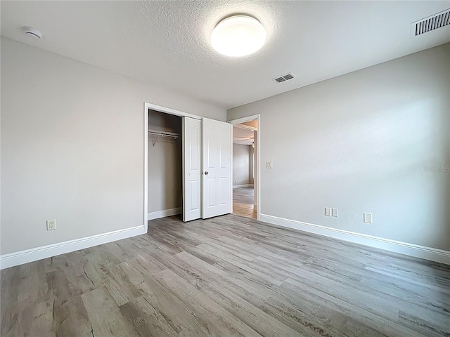 unfurnished bedroom featuring a closet, a textured ceiling, baseboards, visible vents, and wood finished floors