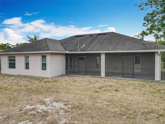 back of house featuring a sunroom, a shingled roof, stucco siding, and a lawn