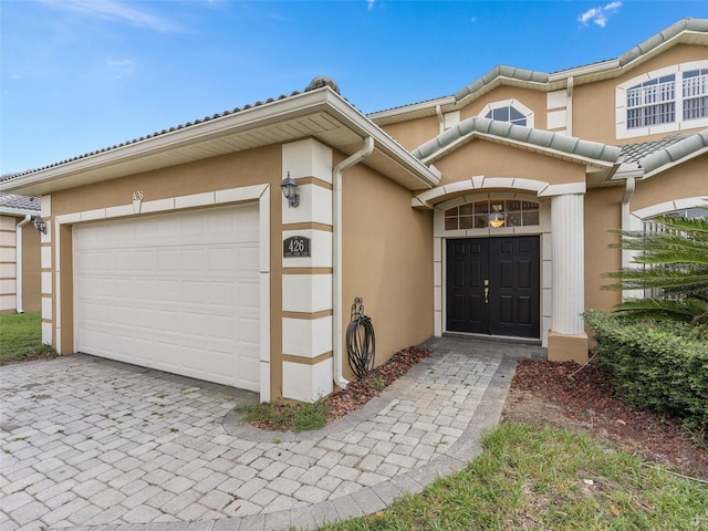 view of exterior entry featuring a garage, stucco siding, and driveway