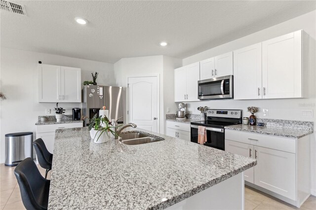 1975 Cacutta Way, Kissimmee, FL 34744 - kitchen featuring stainless steel appliances, a sink, a kitchen island with sink, white cabinets, and light stone counters