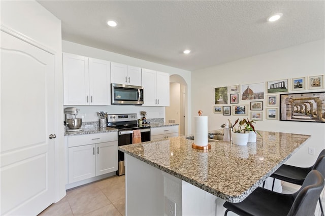 1975 Cacutta Way, Kissimmee, FL 34744 - kitchen with stainless steel appliances, a kitchen breakfast bar, arched walkways, white cabinets, and recessed lighting