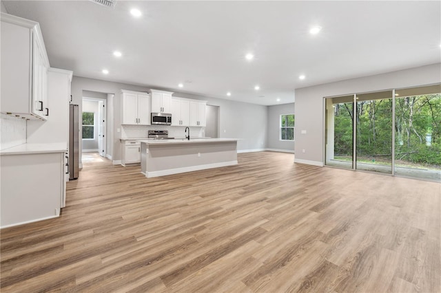 unfurnished living room featuring a sink, recessed lighting, light wood-type flooring, and baseboards