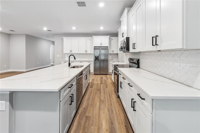 kitchen featuring appliances with stainless steel finishes, a sink, light wood-style floors, recessed lighting, and a center island with sink