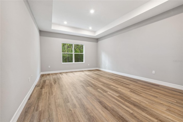 empty room featuring recessed lighting, light wood-type flooring, baseboards, and a raised ceiling