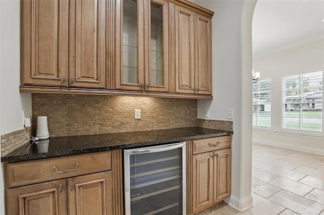 indoor dry bar with wine cooler, tasteful backsplash, arched walkways, and baseboards