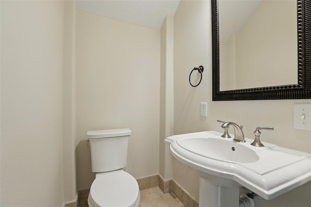 half bathroom with baseboards, toilet, and a sink