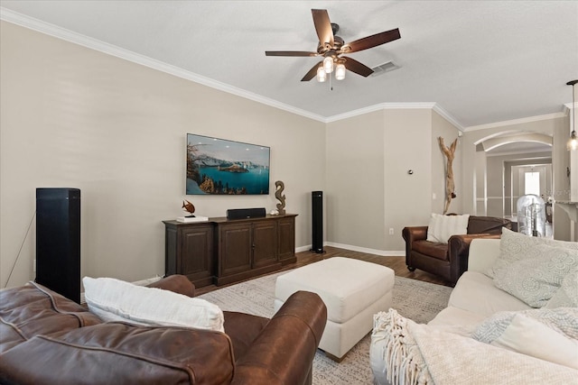 living room featuring baseboards, ornamental molding, visible vents, ceiling fan, and arched walkways