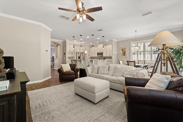 living area featuring a ceiling fan, light wood finished floors, baseboards, arched walkways, and ornamental molding