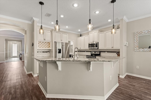 kitchen with appliances with stainless steel finishes, backsplash, arched walkways, a kitchen bar, and recessed lighting