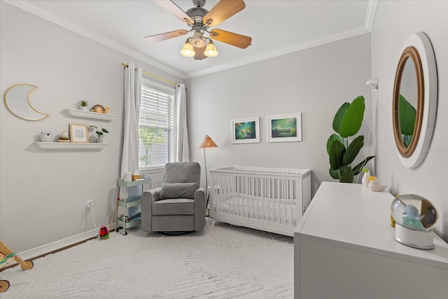 bedroom with a nursery area, crown molding, baseboards, and ceiling fan