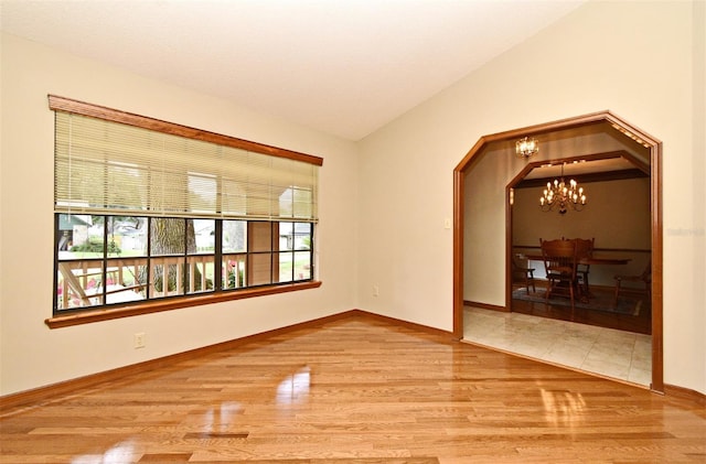 spare room featuring wood finished floors, a chandelier, baseboards, and arched walkways