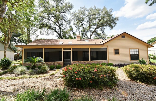 rear view of house featuring a sunroom, a chimney, and brick siding