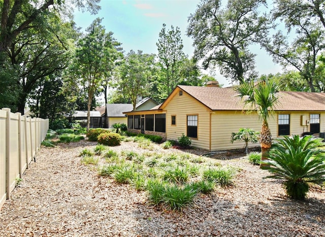 rear view of house with a sunroom, fence, a chimney, and roof with shingles