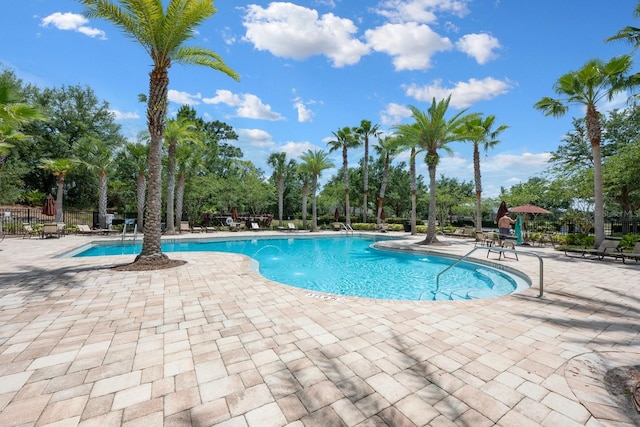 community pool featuring a patio area, view of scattered trees, and fence