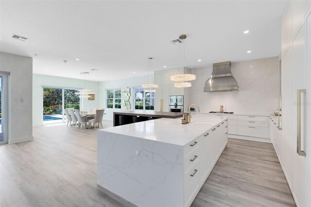 300 Muirfield Loop, Reunion, FL 34747 - kitchen featuring wall chimney range hood, a large island, light wood-style flooring, recessed lighting, and a sink