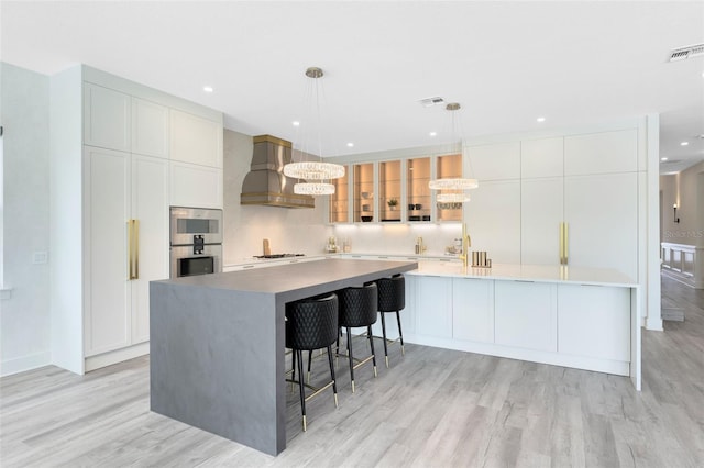 300 Muirfield Loop, Reunion, FL 34747 - kitchen featuring wall chimney range hood, stainless steel double oven, a large island, light wood-style flooring, and white cabinetry