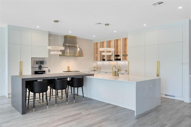 300 Muirfield Loop, Reunion, FL 34747 - kitchen with wall chimney range hood, a spacious island, decorative backsplash, stainless steel double oven, and light wood-type flooring