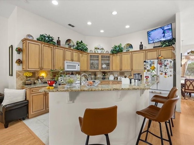 kitchen with white appliances, light wood-type flooring, tasteful backsplash, brown cabinetry, and glass insert cabinets