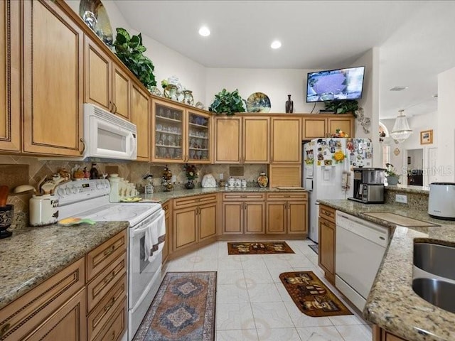 kitchen with white appliances, brown cabinets, tasteful backsplash, light stone counters, and glass insert cabinets