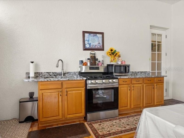 kitchen with appliances with stainless steel finishes, a sink, stone countertops, and brown cabinetry