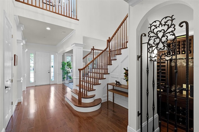 entryway featuring hardwood / wood-style floors, stairway, a towering ceiling, a decorative wall, and ornamental molding