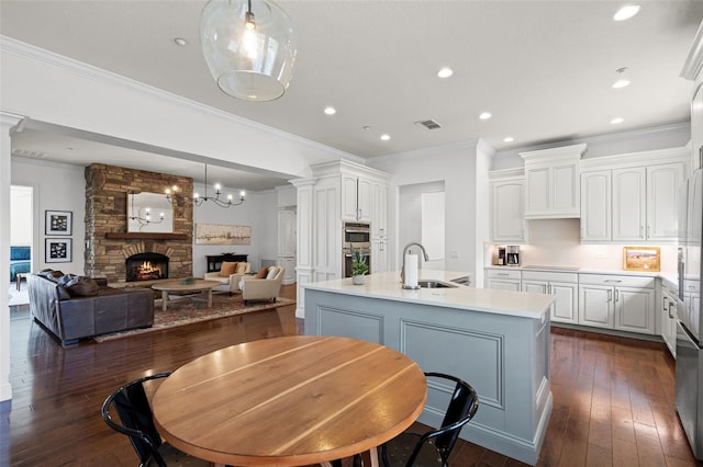 kitchen with a sink, a kitchen island with sink, white cabinets, crown molding, and open floor plan
