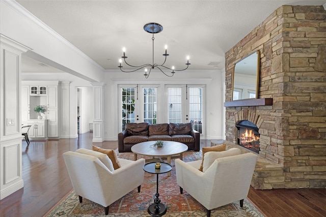 living room featuring wood finished floors, a chandelier, a stone fireplace, crown molding, and baseboards