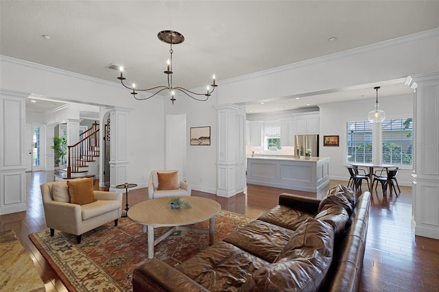 living room with decorative columns, hardwood / wood-style flooring, ornamental molding, stairway, and a chandelier