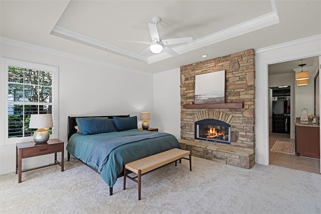 carpeted bedroom with a tray ceiling, crown molding, a fireplace, a ceiling fan, and ensuite bathroom