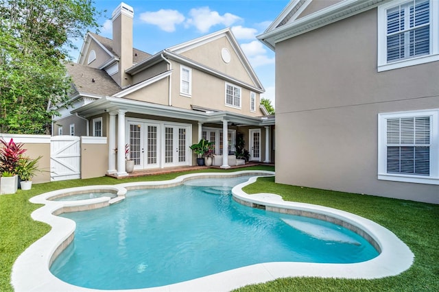 rear view of property featuring french doors, stucco siding, a gate, a chimney, and a pool with connected hot tub