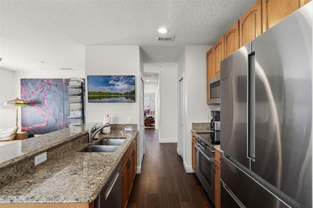 kitchen with stainless steel appliances, a sink, light stone countertops, a textured ceiling, and dark wood-style floors