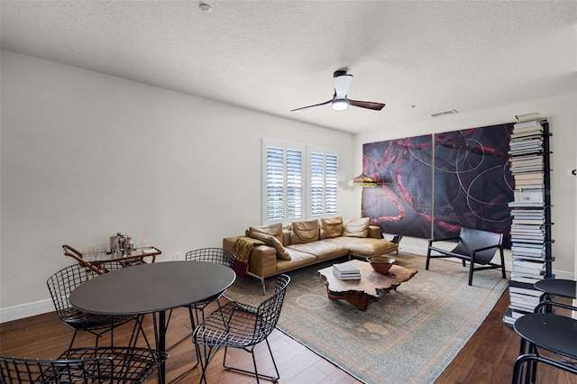 living area with a ceiling fan, wood finished floors, baseboards, and a textured ceiling