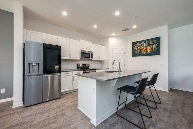 kitchen with stainless steel appliances, a sink, a center island with sink, white cabinetry, and a breakfast bar area