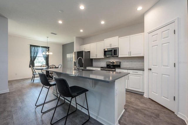 kitchen with appliances with stainless steel finishes, an island with sink, decorative backsplash, a sink, and white cabinets