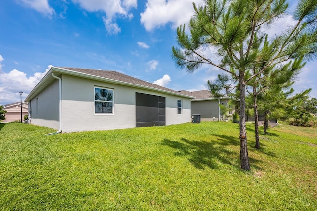 back of house with stucco siding, a lawn, and central AC