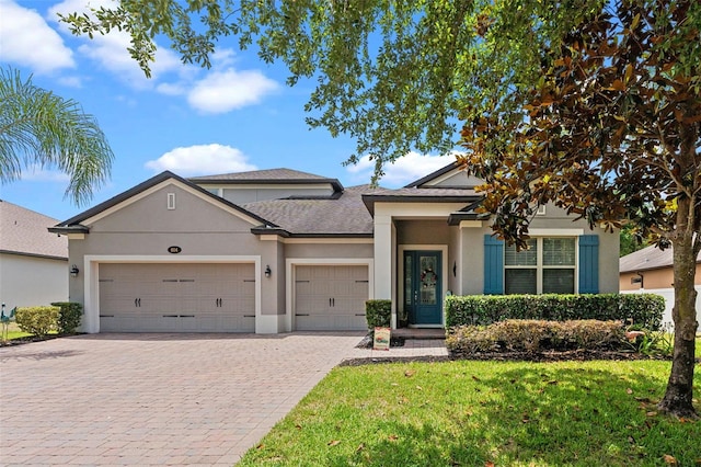 view of front of home with an attached garage, decorative driveway, stucco siding, a front yard, and roof with shingles