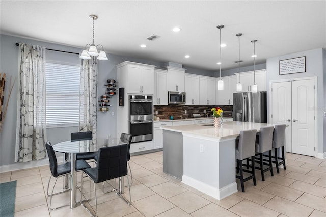 kitchen with stainless steel appliances, tasteful backsplash, a kitchen island with sink, light countertops, and recessed lighting