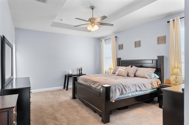 bedroom with light colored carpet, a ceiling fan, baseboards, and a tray ceiling